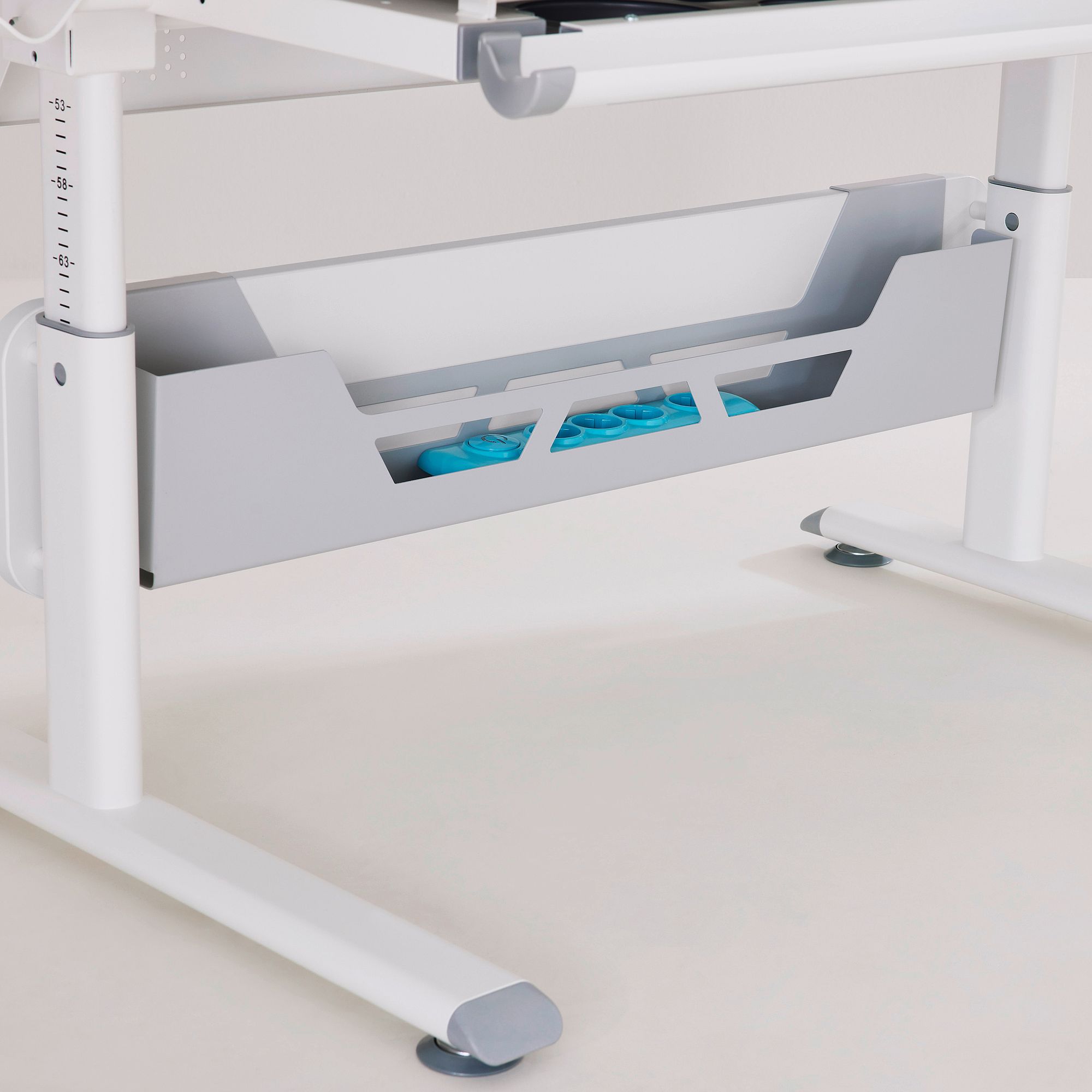 Gray desk storage tray with blue objects underneath a white adjustable desk.