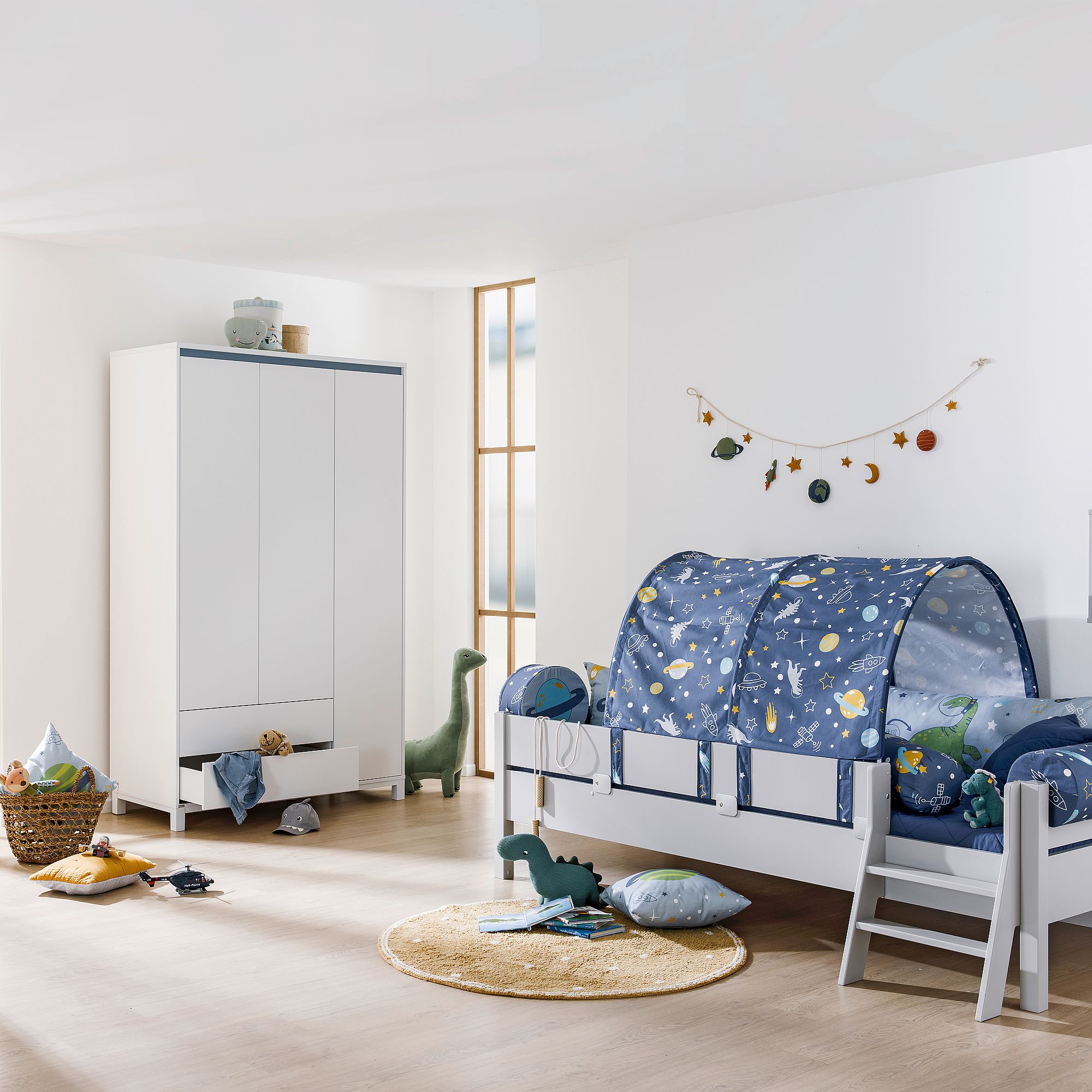 Kinderzimmer mit einem Bettzelt im Weltraum-Design, Spielzeug, einem Kleiderschrank und sanfter Beleuchtung.