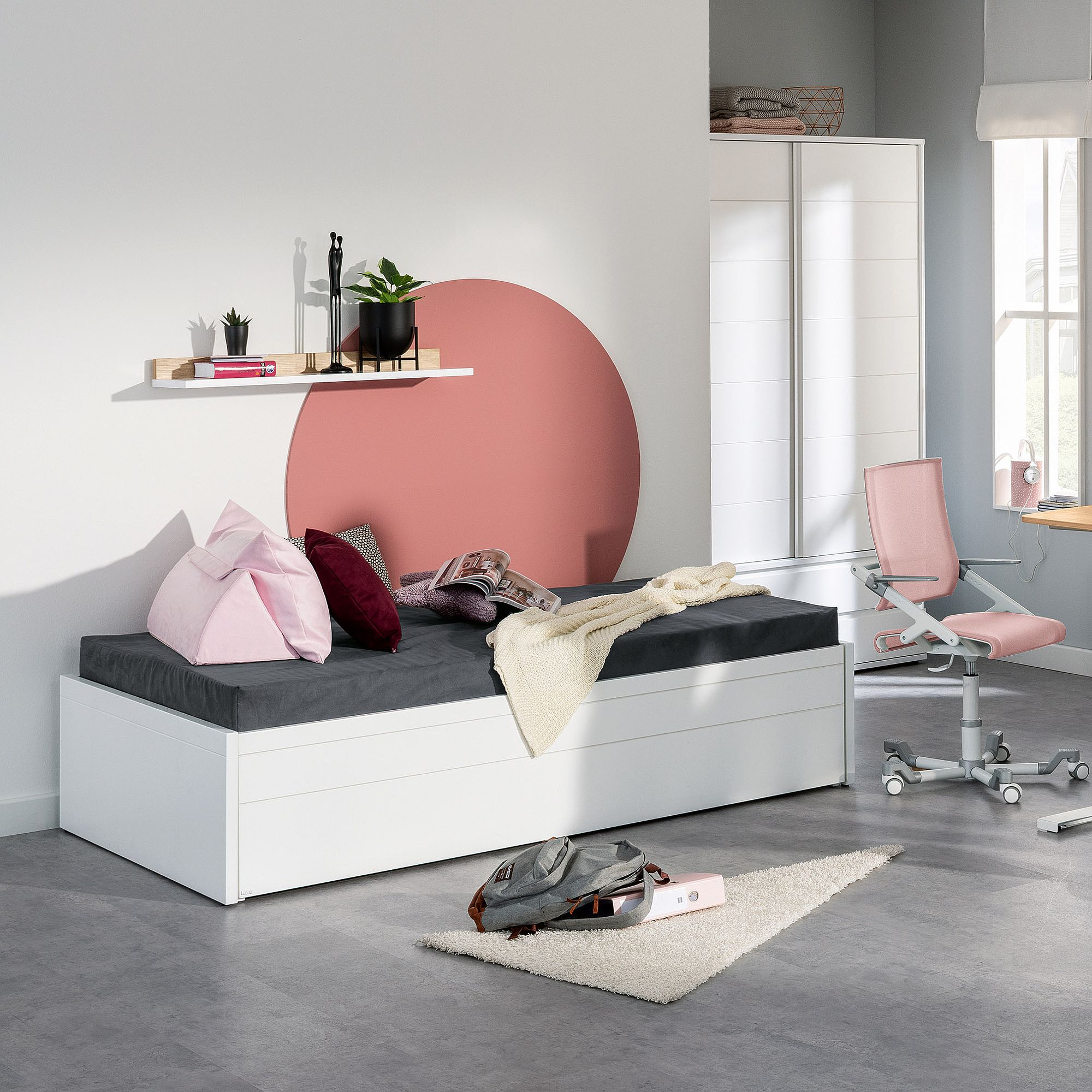 Modernes Schlafzimmer mit weißem Bett, rosa Stuhl und dekorativem rosa Kreis an der Wand.