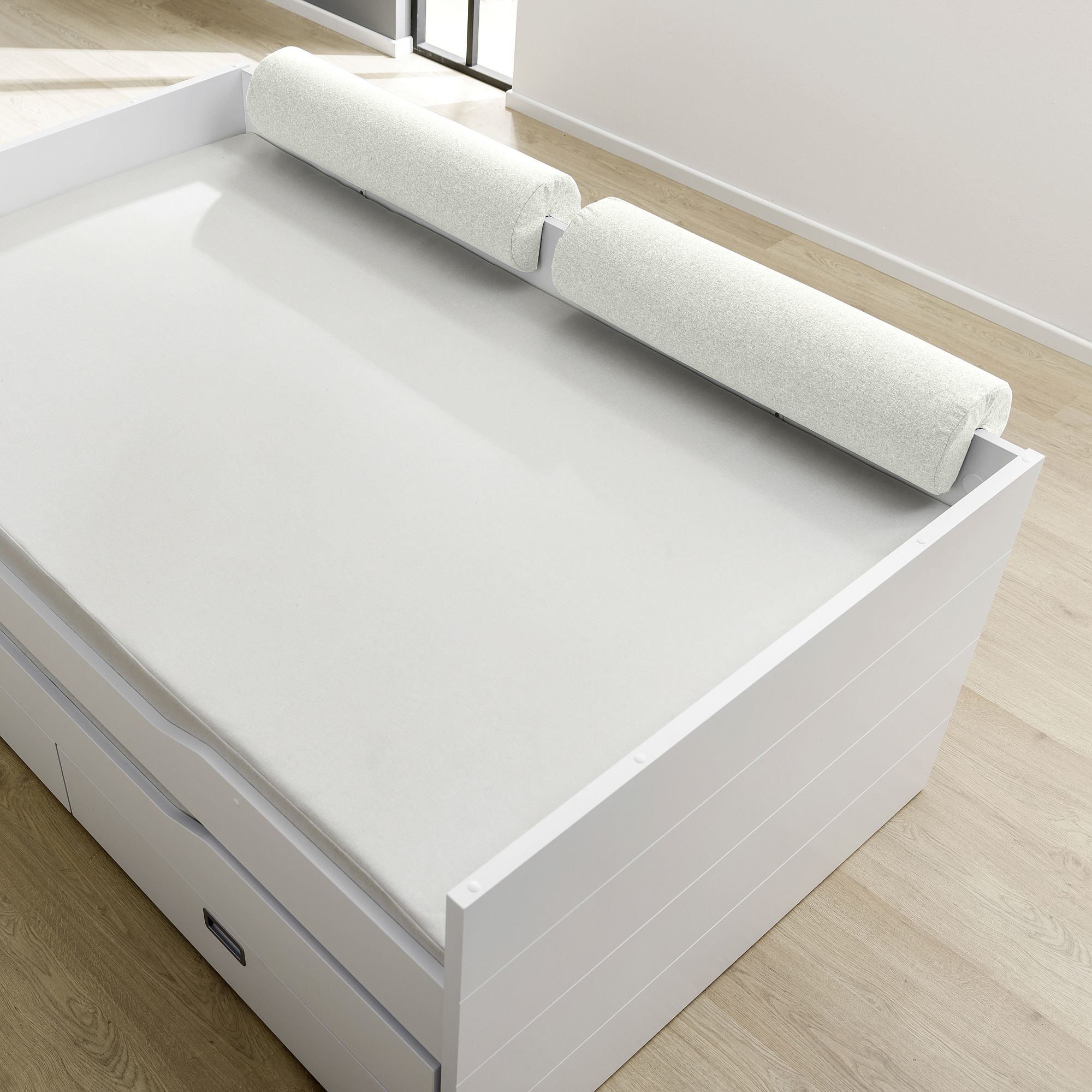 White bed with two cylindrical foam bumpers on the side, in a bright room.
