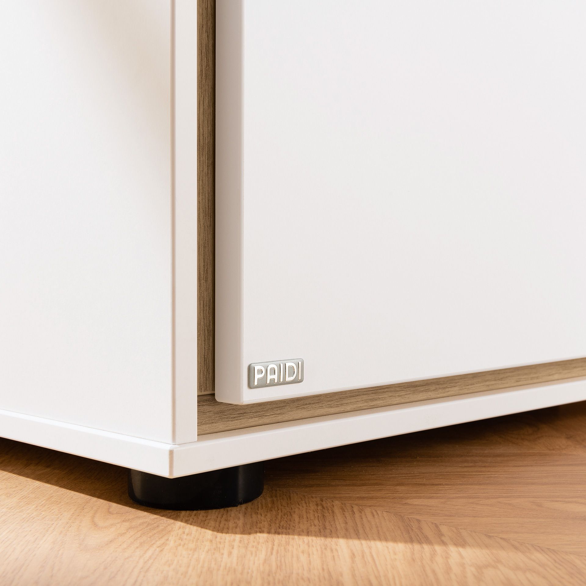 Nahaufnahme einer weißen Schrankecke mit einem PAIDI-Etikett auf einem Holzboden.