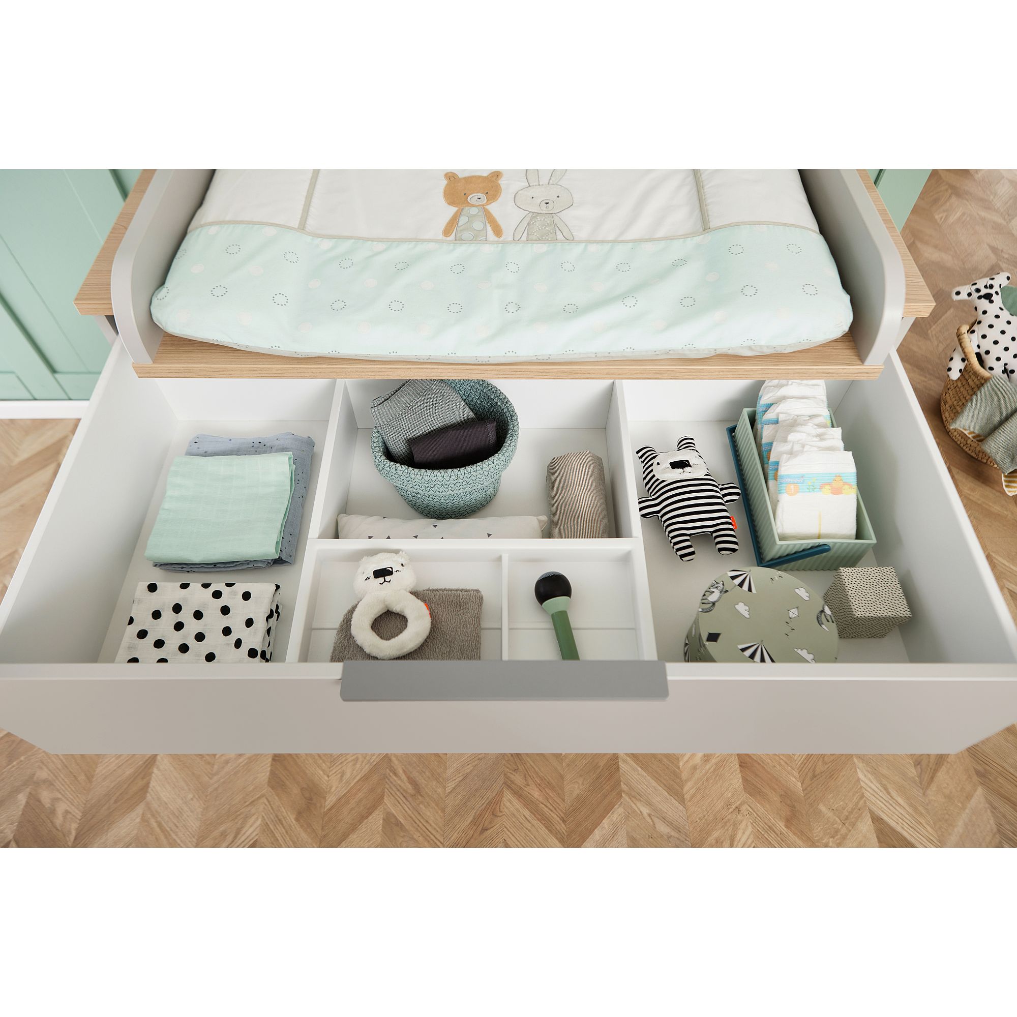 Open drawer with neatly organized baby clothes, toys, and diaper changing items.
