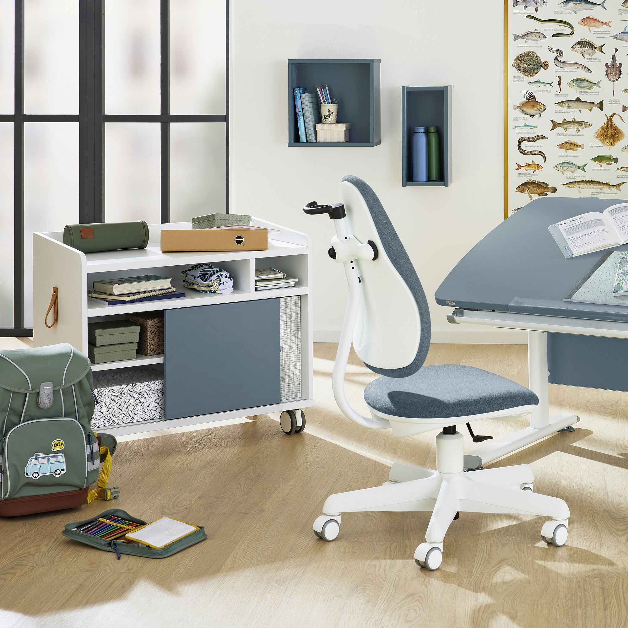 Rollcontainer Rollcaddy mit 1 Schiebetür in Mattblau Moderner Schreibtisch mit Stuhl, Büchern und Schulsachen in einem hellen Raum.