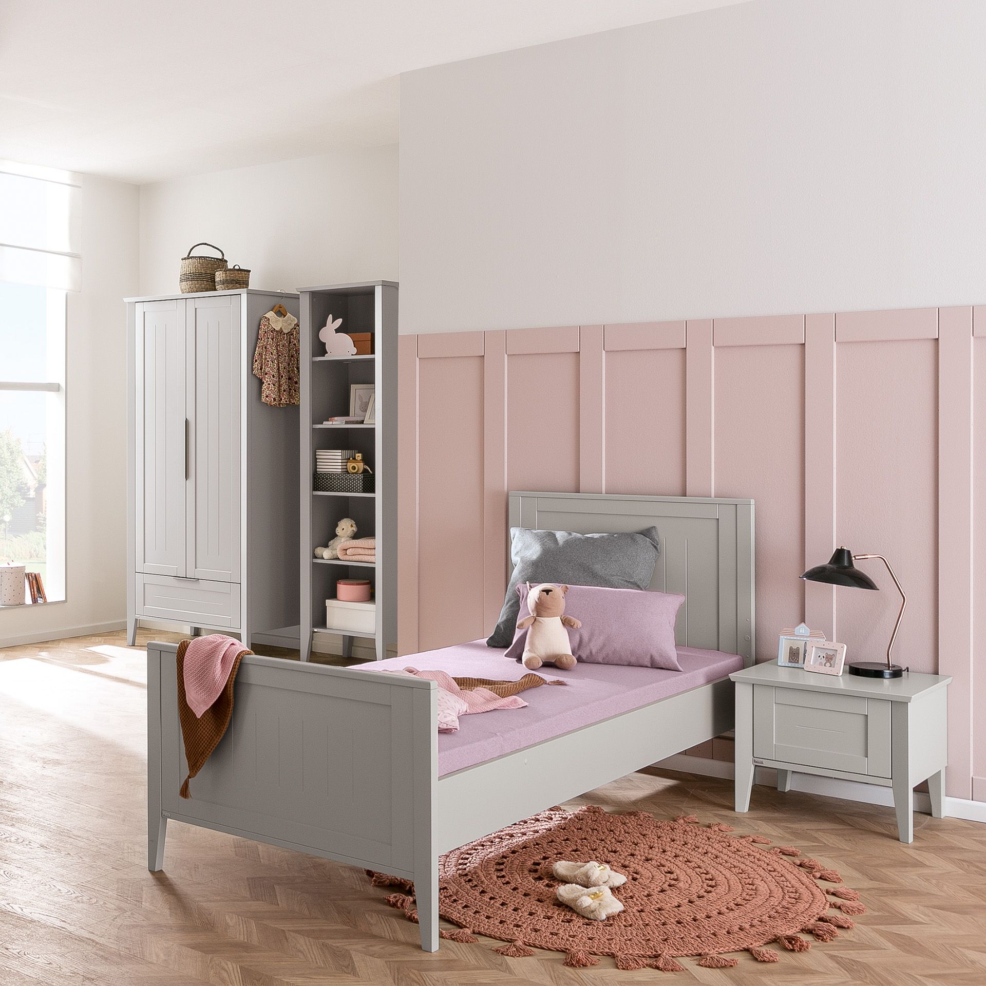 Children’s bedroom with a gray bed, pink bedding, toys, and pastel decor.