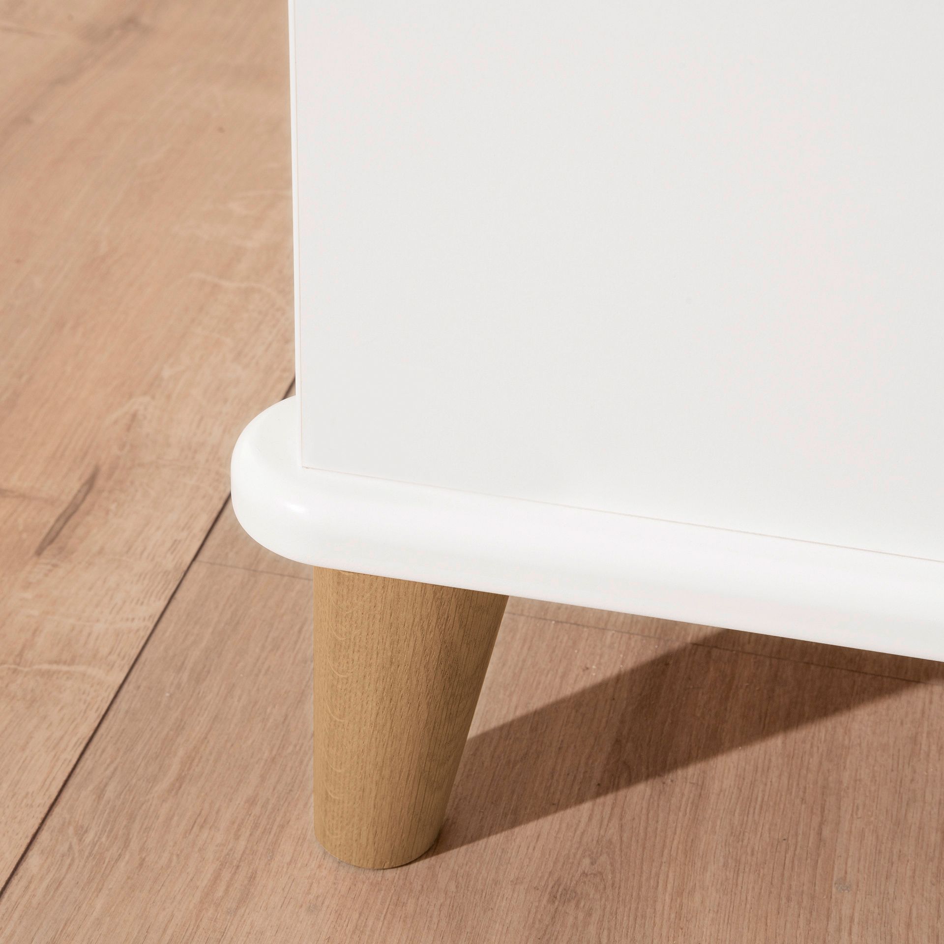 Nahaufnahme eines weißen Schranks mit Holzbeinen auf einem hellen Holzboden.