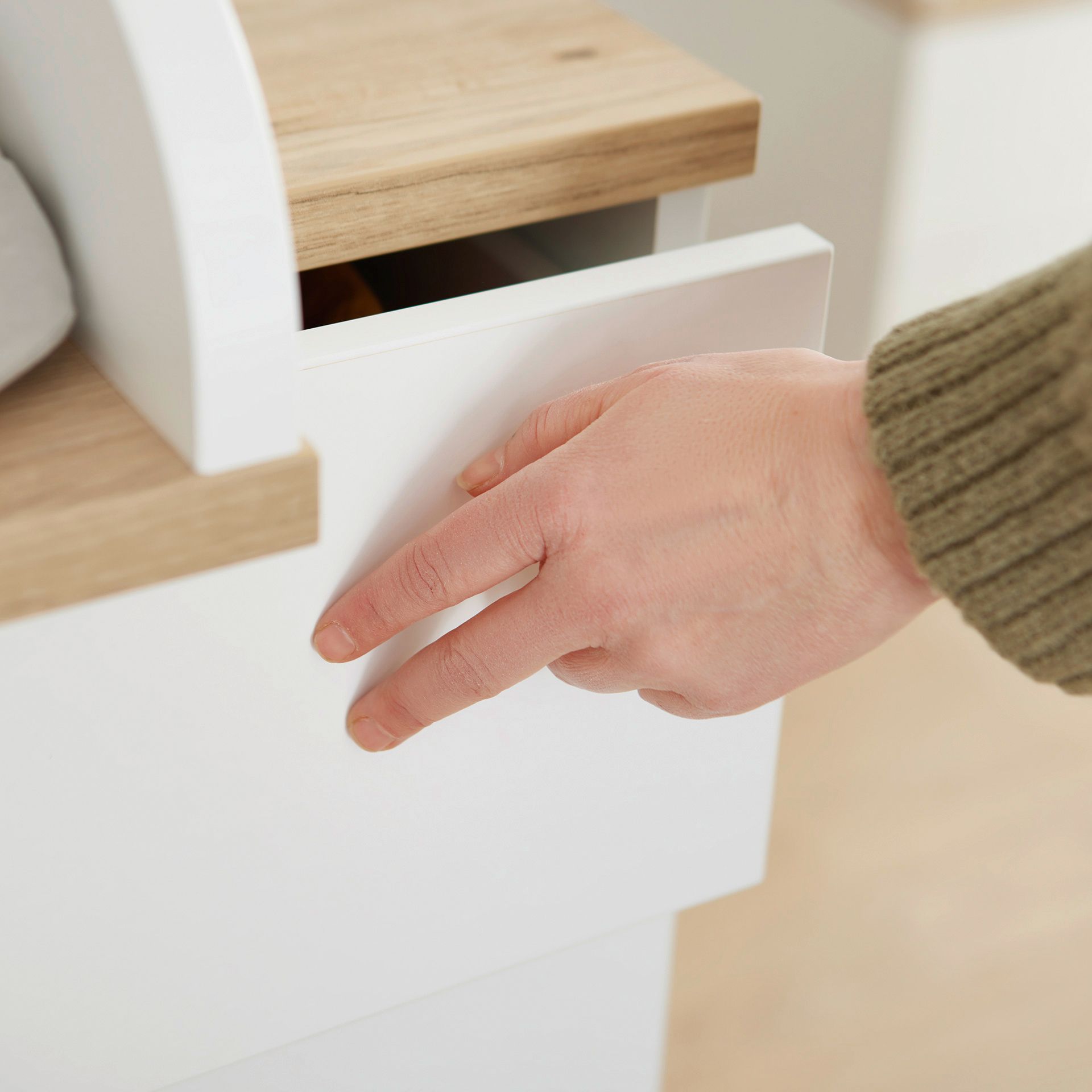 A hand in a green sleeve is opening a white drawer with a wood top.