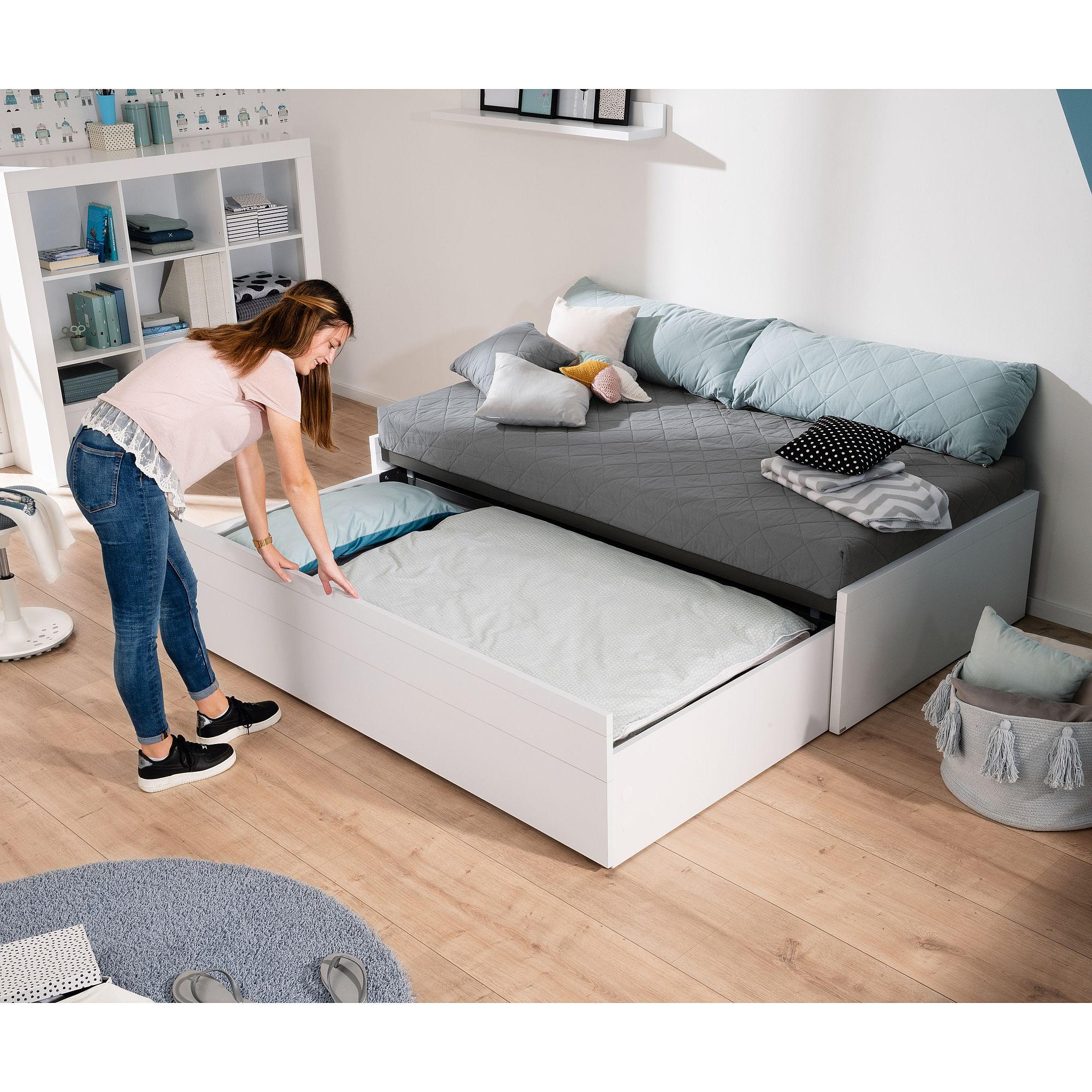 Frau, die in einem modernen, aufgeräumten Schlafzimmer ein Rollbett auszieht.