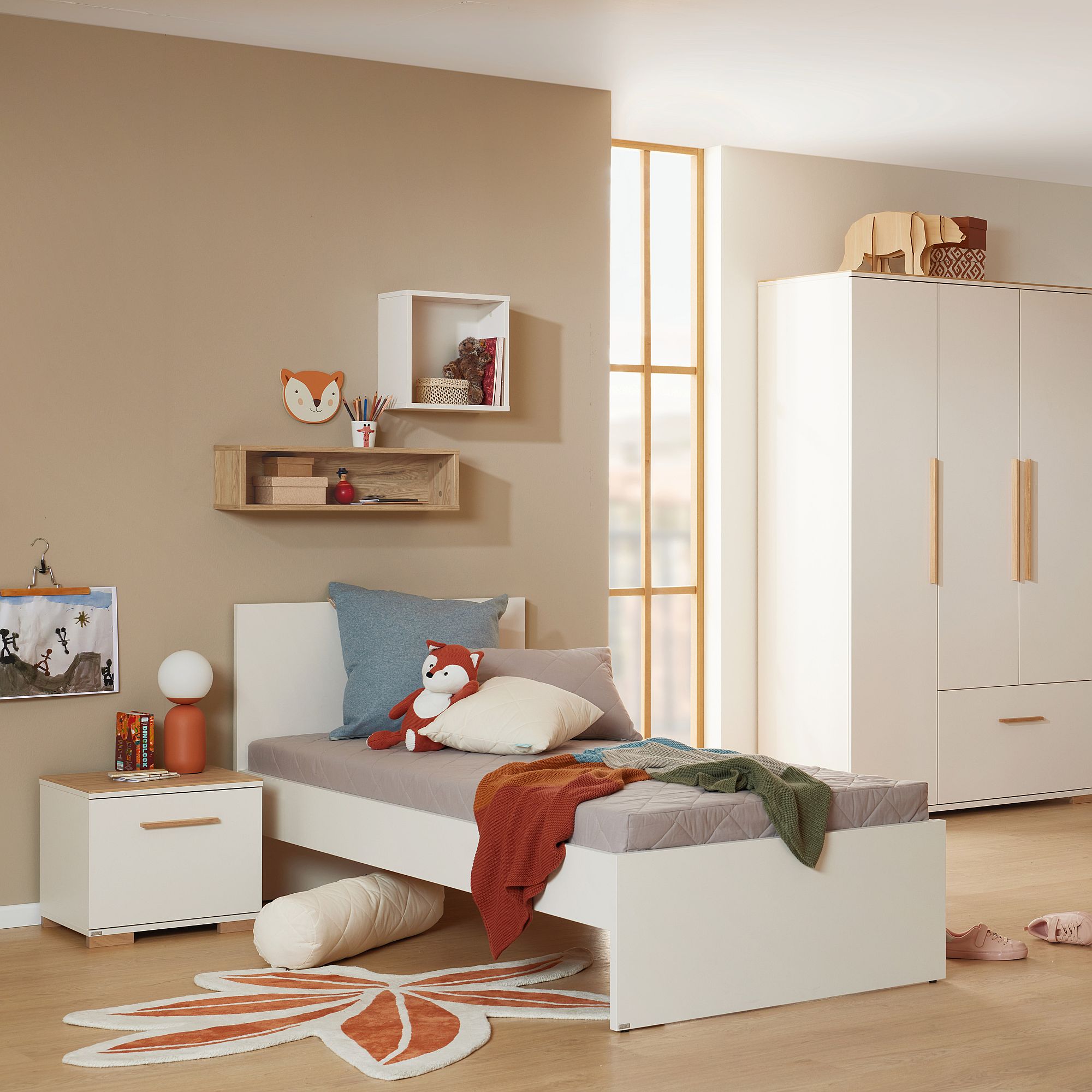 Ein gemütliches Kinderzimmer mit einem Bett, Kissen, Regalen und einem Fuchsteppich.