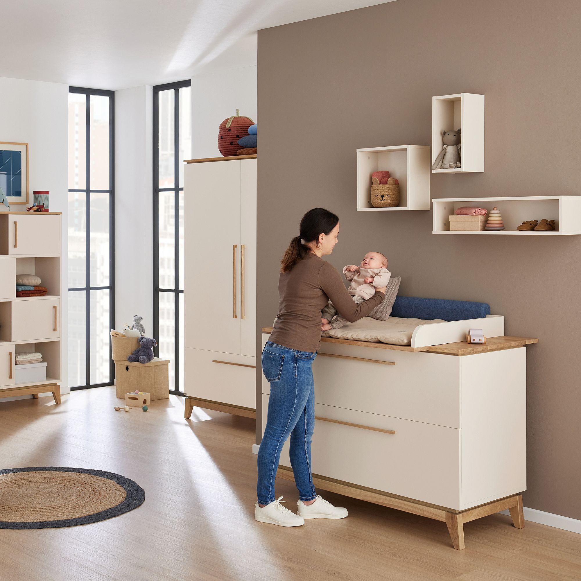 Frau wickelt ein Baby auf einer Kommode in einem modernen, hellen Kinderzimmer.