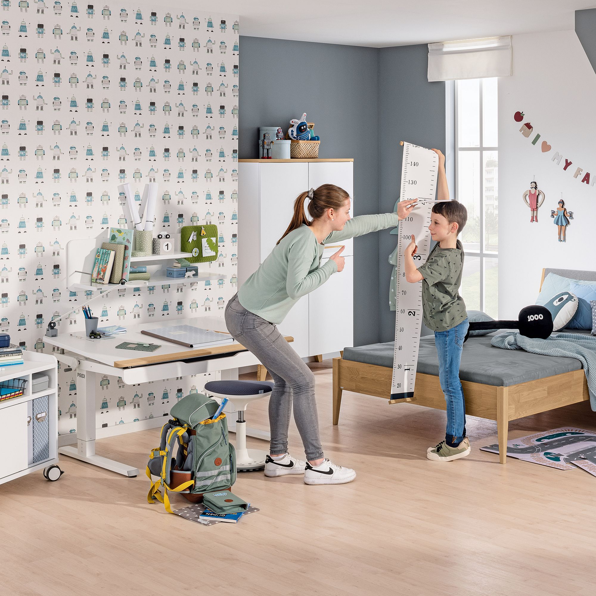 Eine Frau misst die Größe eines lächelnden Jungen in einem Kinderzimmer.