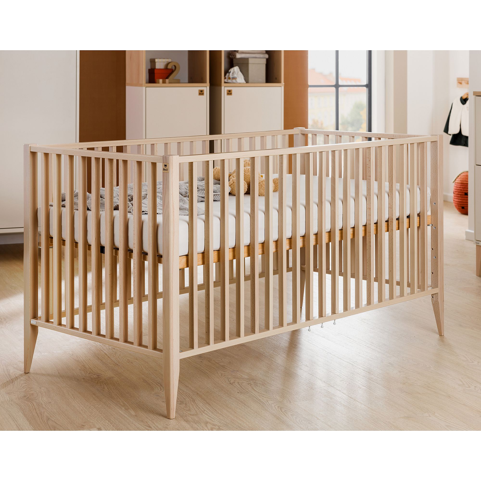 Babybett aus hellem Holz in einem modernen Kinderzimmer mit weichem natürlichem Licht.