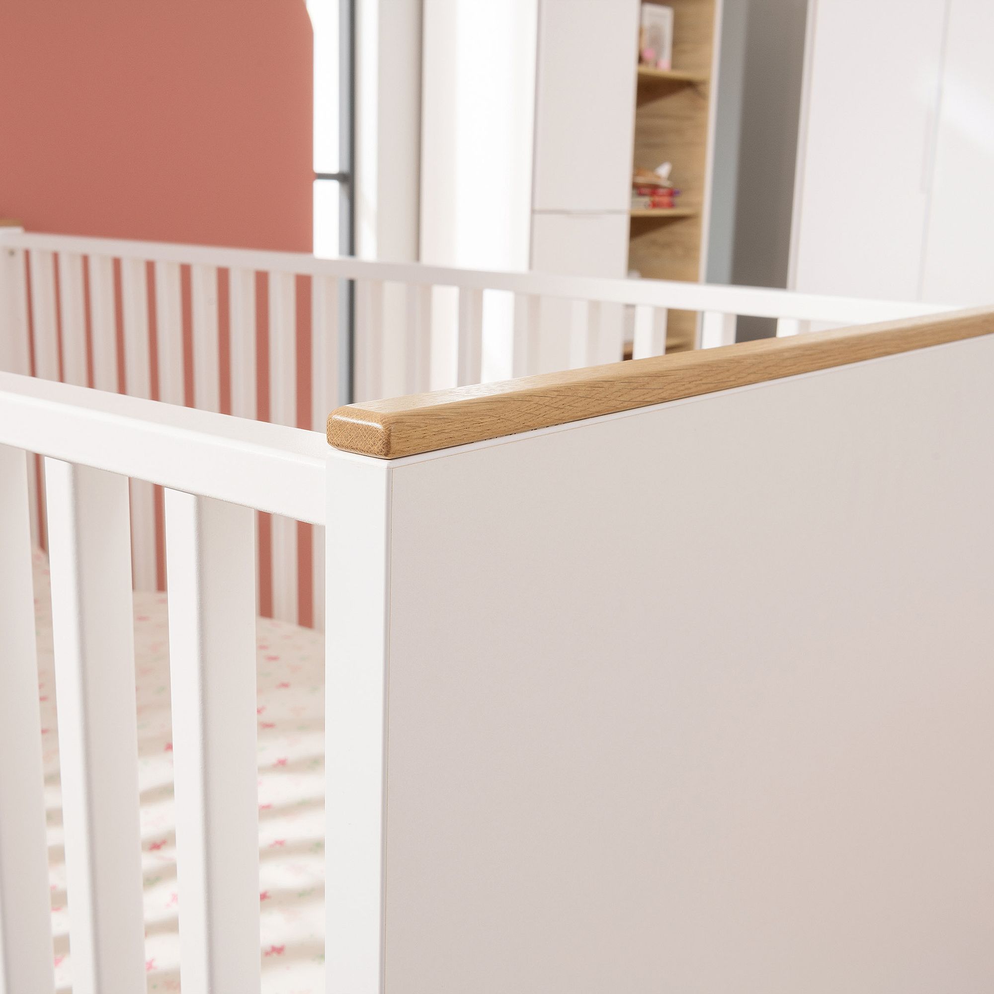 Weißes Babybett mit Holzverkleidung in einem sanft beleuchteten Kinderzimmer.