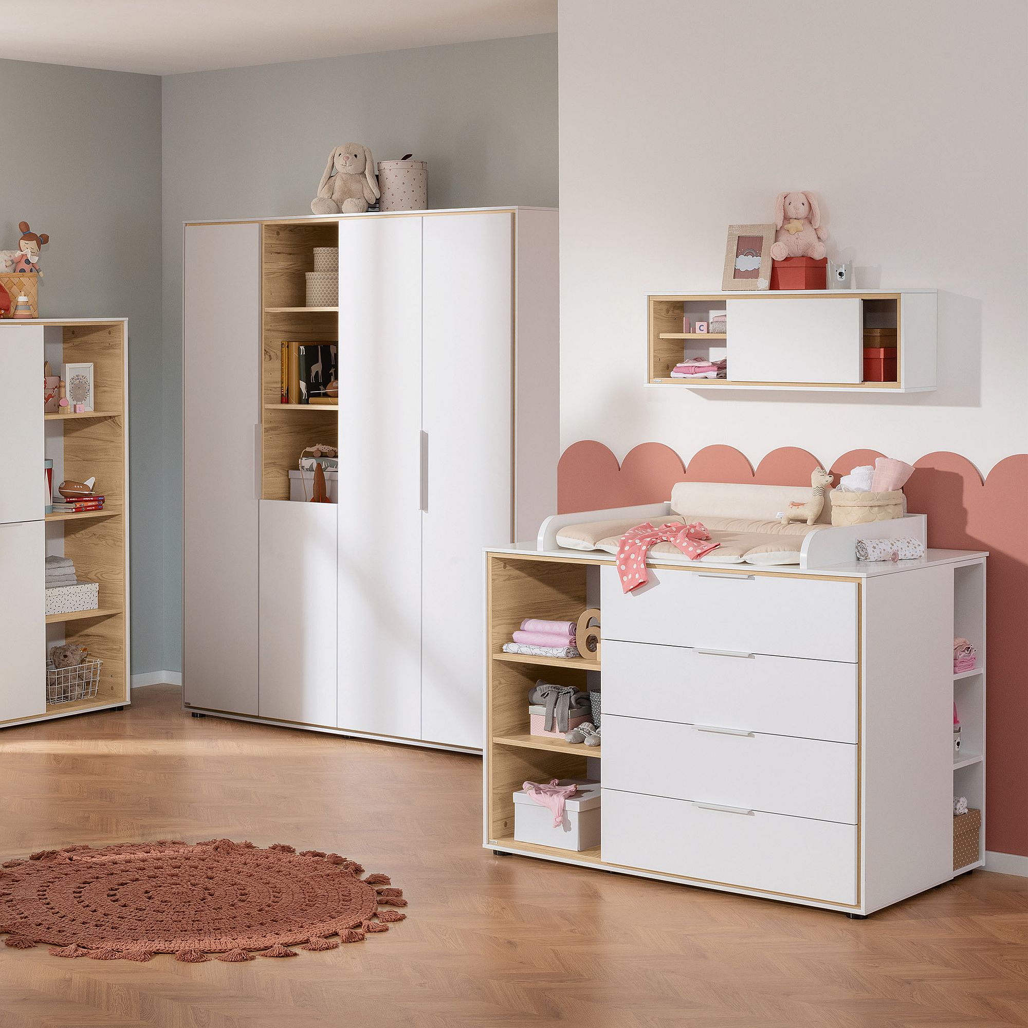 Ein aufgeräumtes Kinderzimmer mit weißen Möbeln, rosa Akzenten und Teddybären auf Regalen.