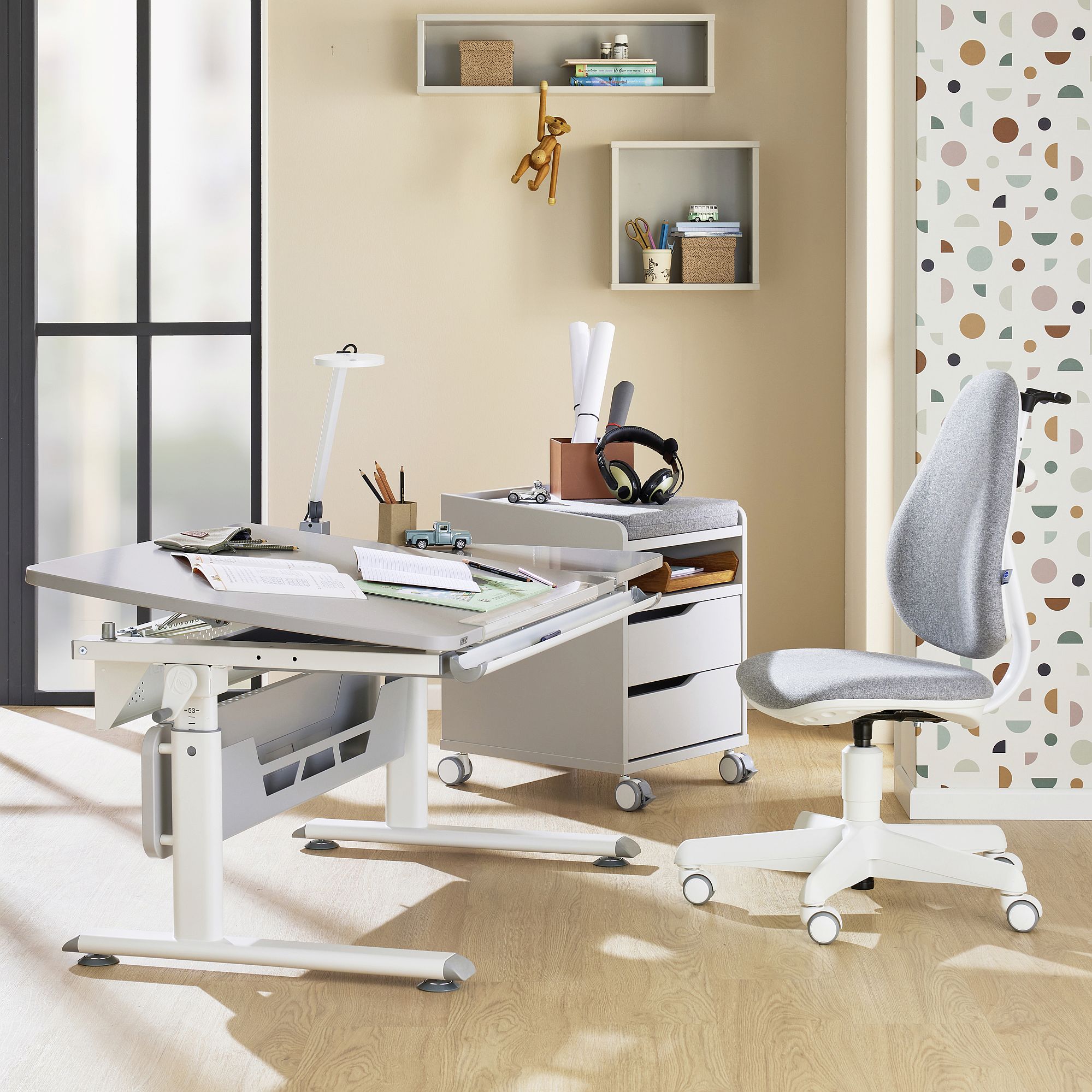 Schülerschreibtisch Diego GT Curved 130 x 70 cm, Kieselgrau Modern home office with a grey chair, desk, shelves, and sunlight streaming in.
