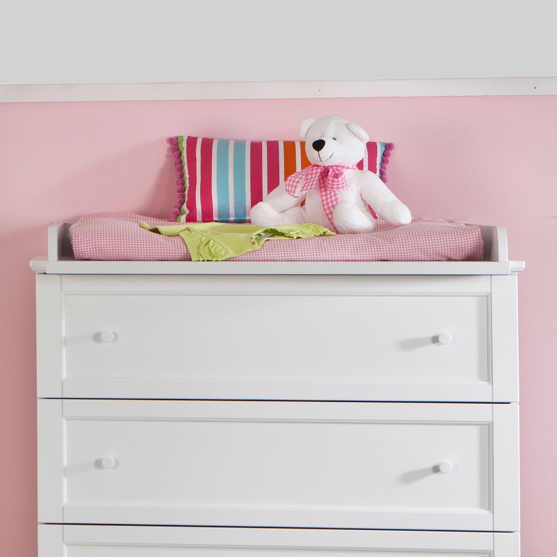 Wickelaufsatz Sophia für Wickelkommode schmal Weiße Kommode mit gestreiftem Kissen, Teddybär und rosa Wickelauflage.