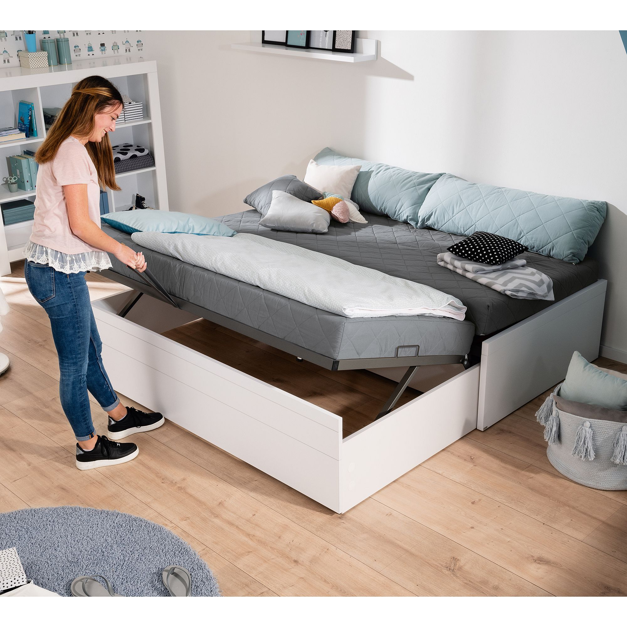 Frau hebt Matratze auf einem weißen Stauraumbett in einem modernen Schlafzimmer.