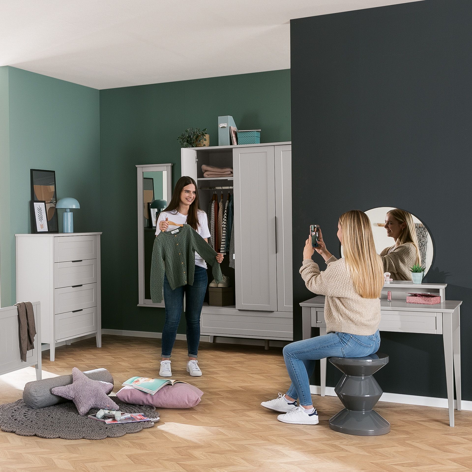 Two women in a bedroom, one holding a shirt, the other taking a photo.