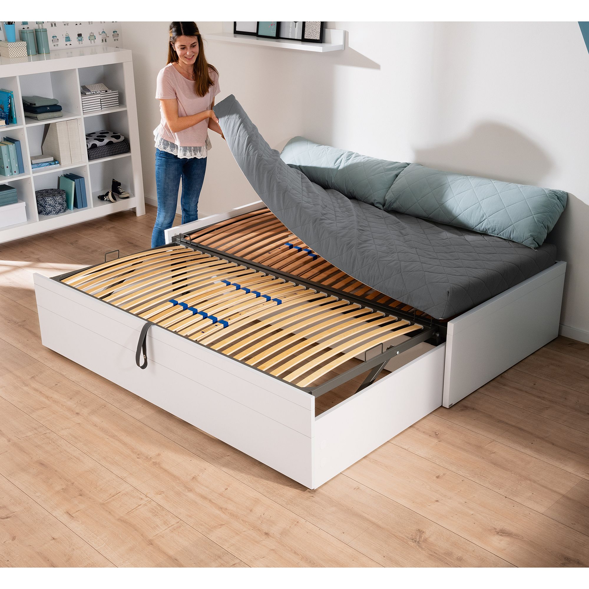 Eine Frau hebt die Matratze an, um den Stauraum unter einem modernen weißen Bettrahmen freizulegen.