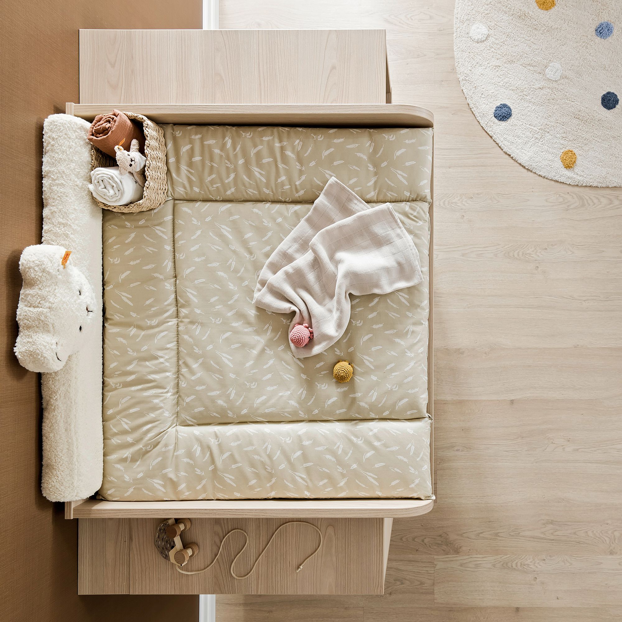 Beigefarbener Wickeltisch mit einer Decke, Spielzeug und einem Korb mit gerollten Handtüchern.