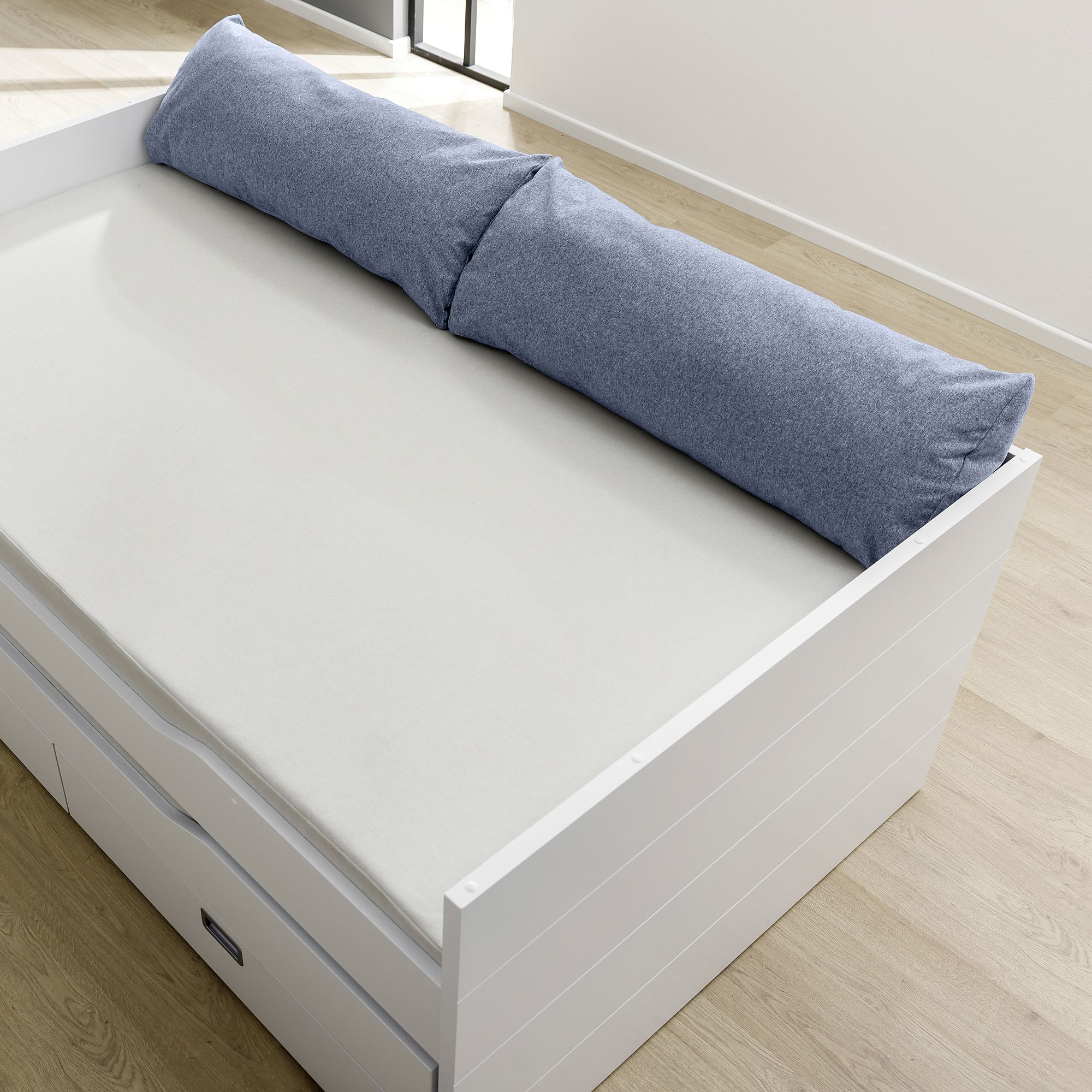 White daybed with storage drawers, topped with a cream mattress and blue pillows.