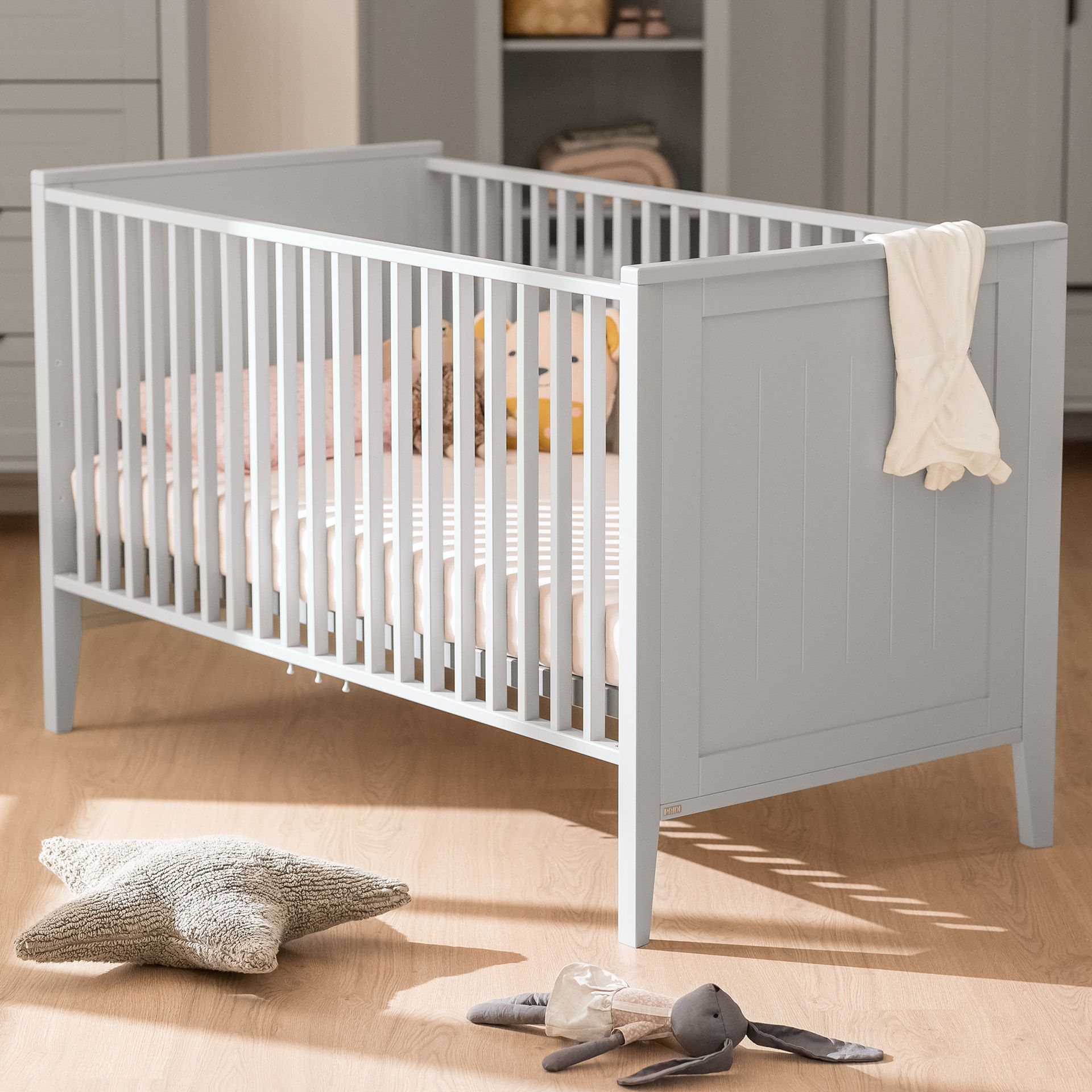 Babybett Levke 70 x 140 cm Hellgraues Kinderbett mit einer weißen Decke, die über die Seite in einem gemütlichen Kinderzimmer drapiert ist.