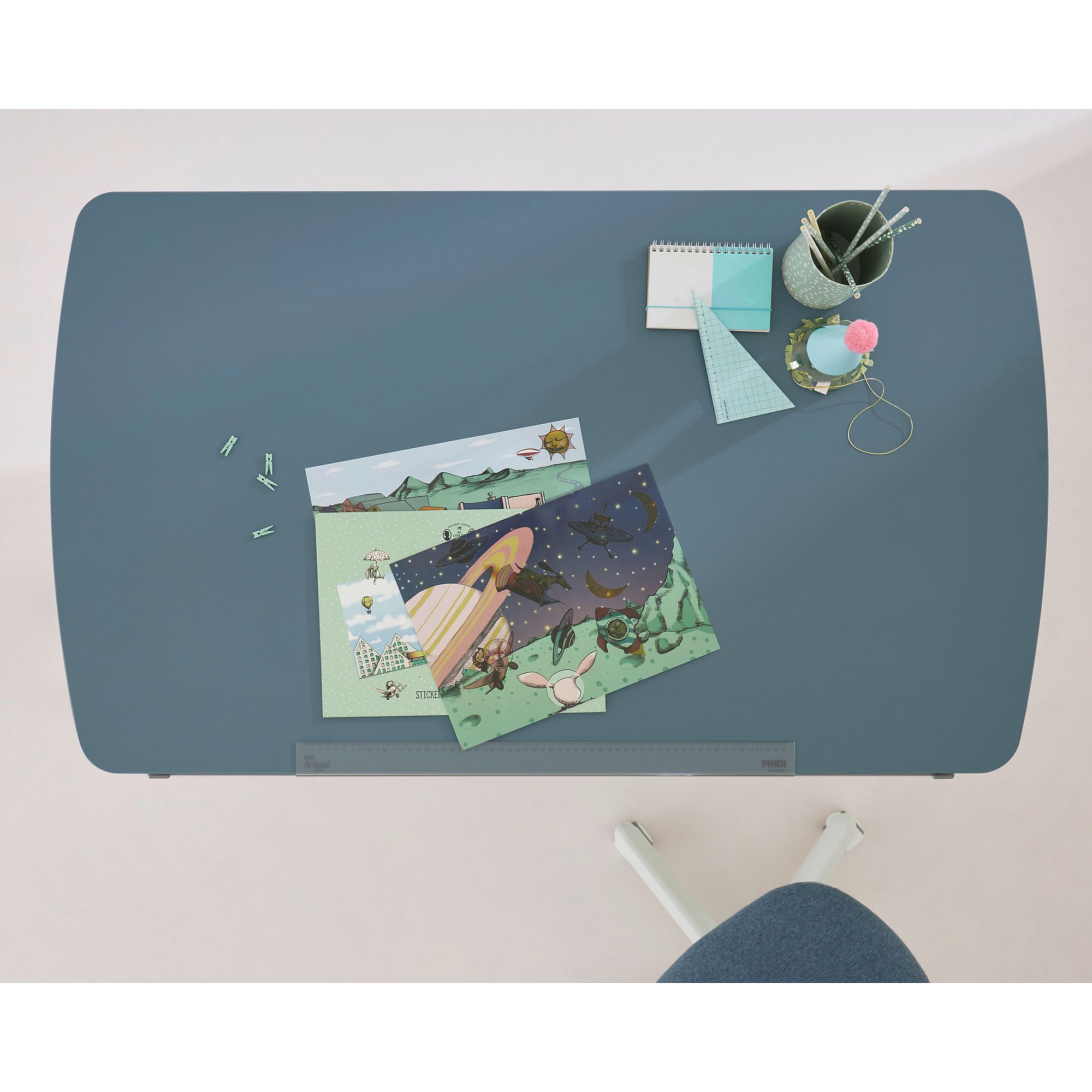 Schülerschreibtisch Diego Curved 120 x 70 cm in Mattblau Ein blauer Schreibtisch mit Zeichnungen, Schreibwaren und einem Stuhl von oben gesehen.