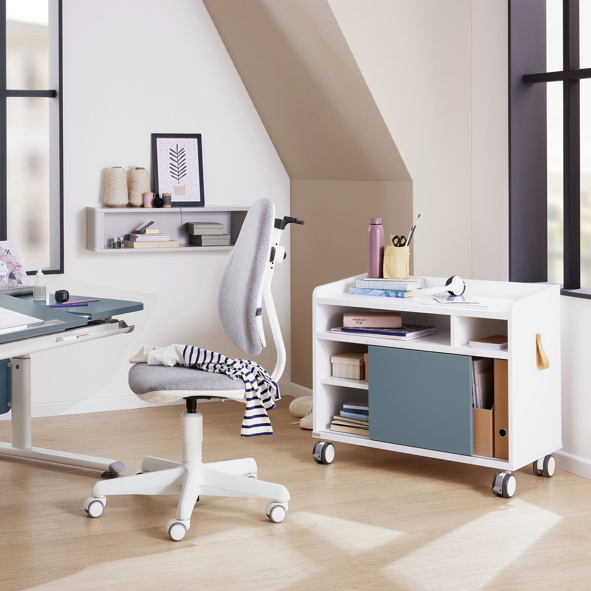 Modernes Heimbüro mit grauem Stuhl, Schreibtisch und Aufbewahrungswagen in der Nähe großer Fenster.