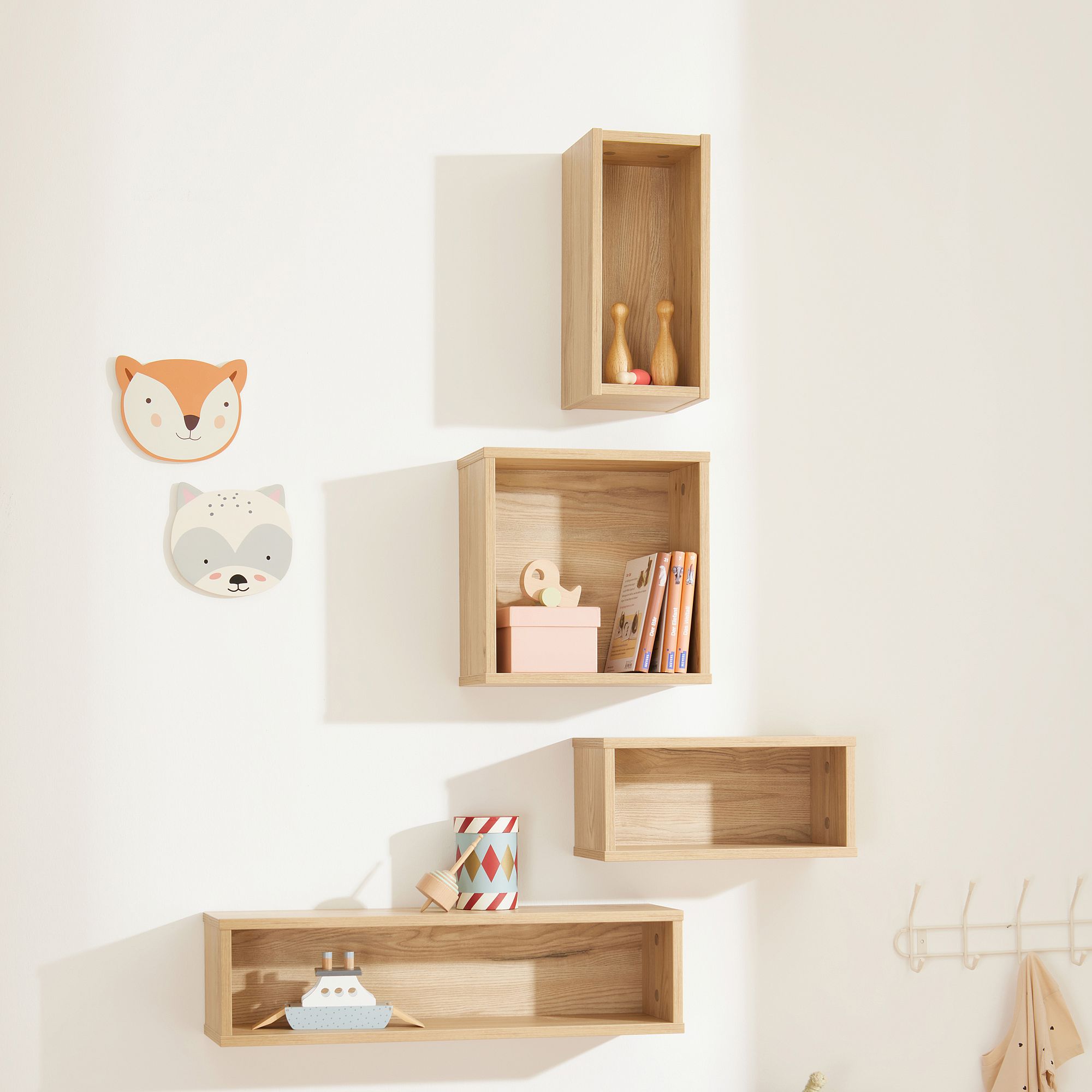 Vier hölzerne Wandregale mit Spielzeug, Büchern und tierischem Wandschmuck an einer weißen Wand.