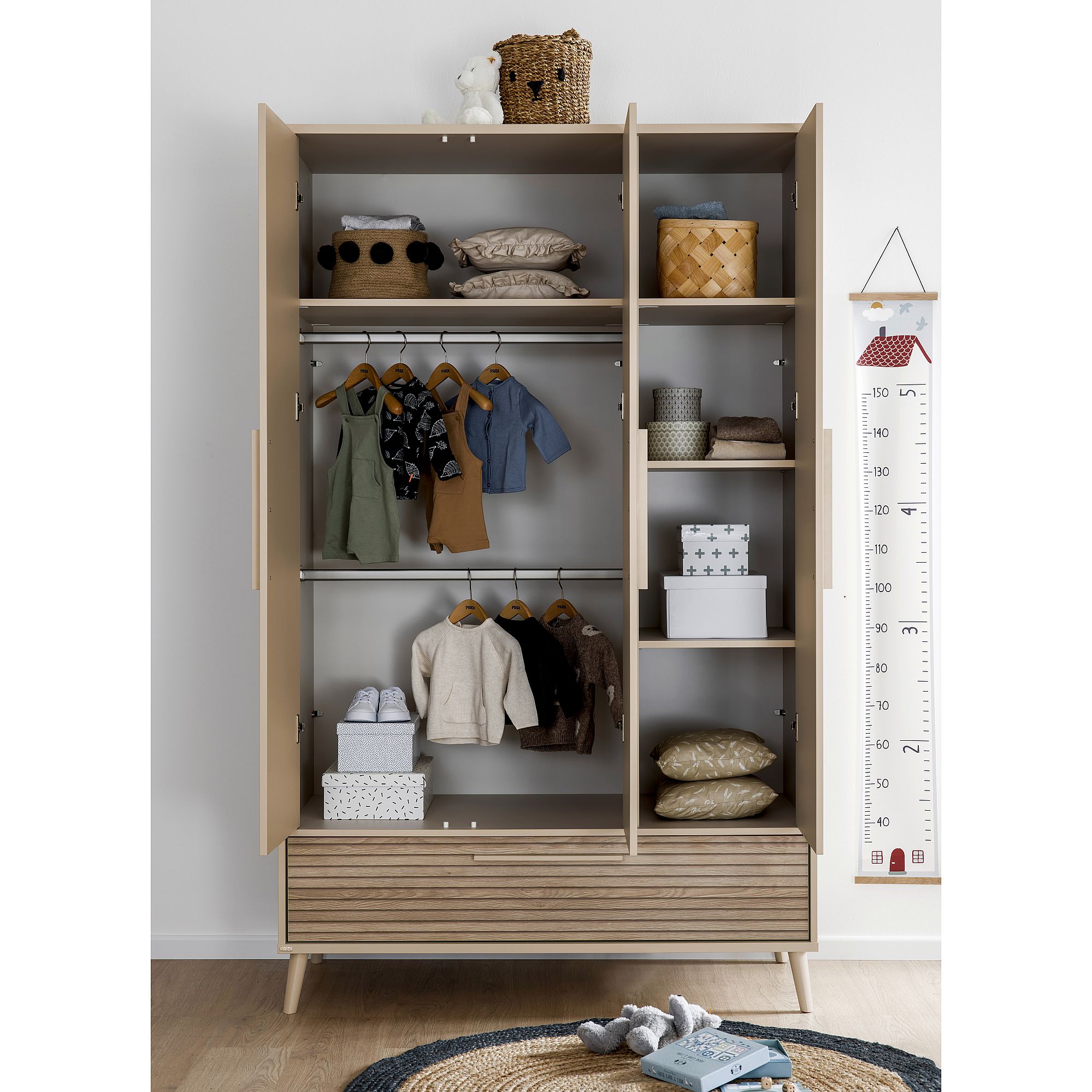 Offener Kleiderschrank mit Kinderkleidung, Körben, Kissen und Plüschtieren darin.