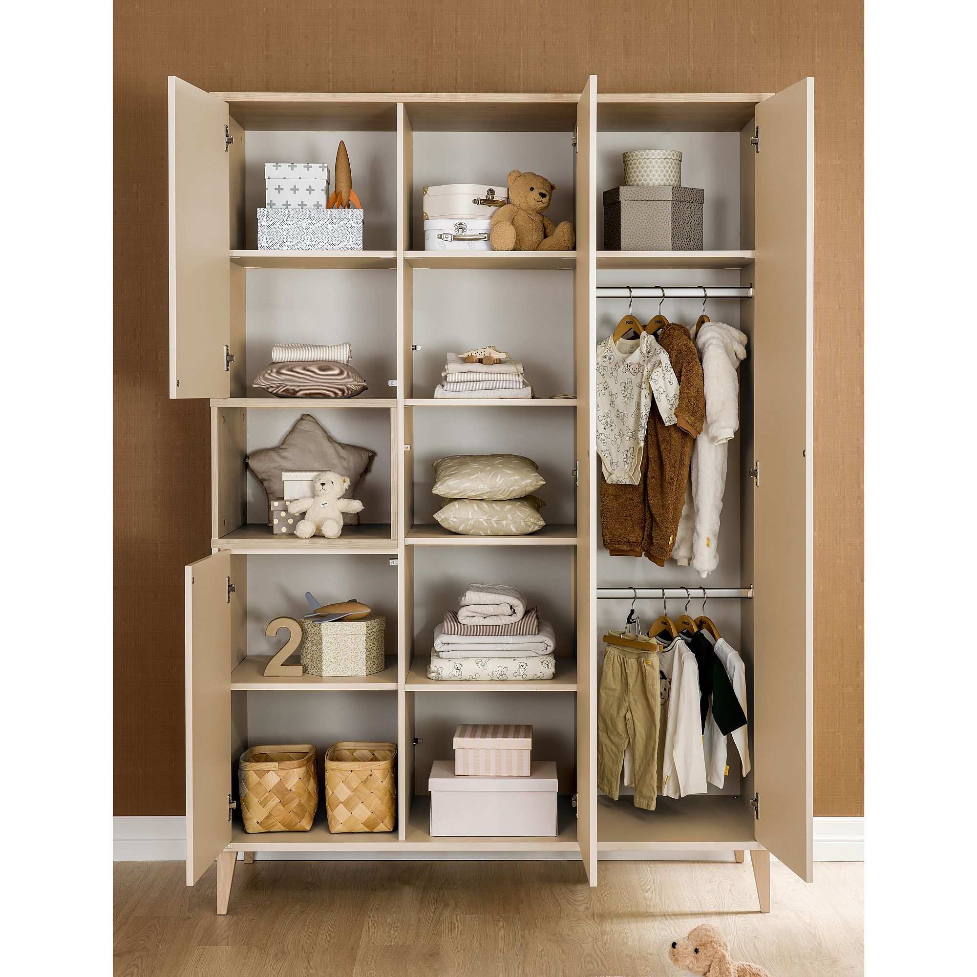 Beigefarbene Garderobe mit Regalen, Körben, Kleidung, Kissen und Stofftieren.