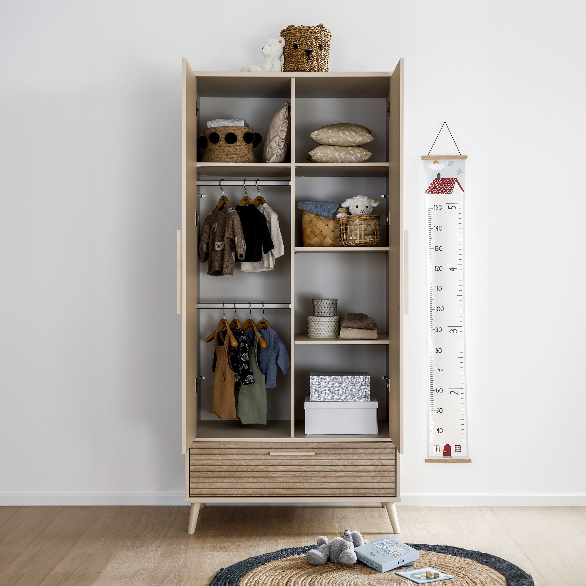 Ein Kinderschrank mit Kleidung, Regalen und Aufbewahrungskörben, daneben eine Wachstumstabelle.