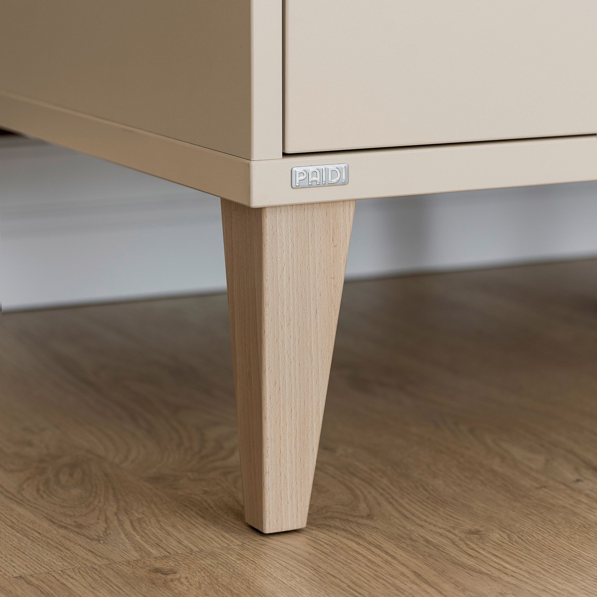 Nahaufnahme eines Schrankbeins aus Holz auf einem Hartholzboden, mit einem PAIDI-Etikett.
