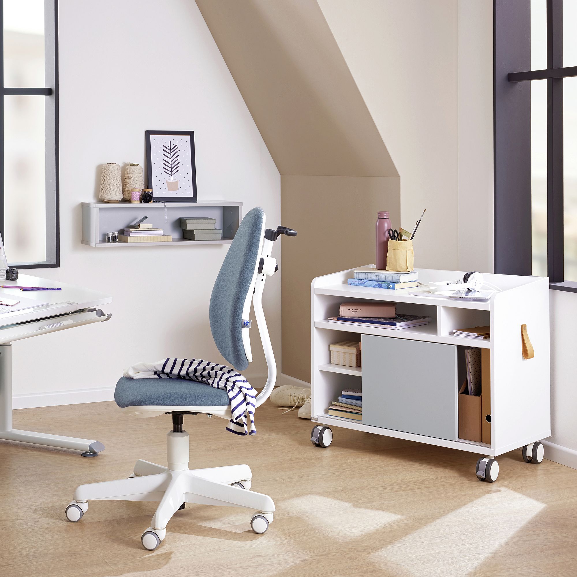 Modern home office with a white desk, blue chair, and rolling storage unit.