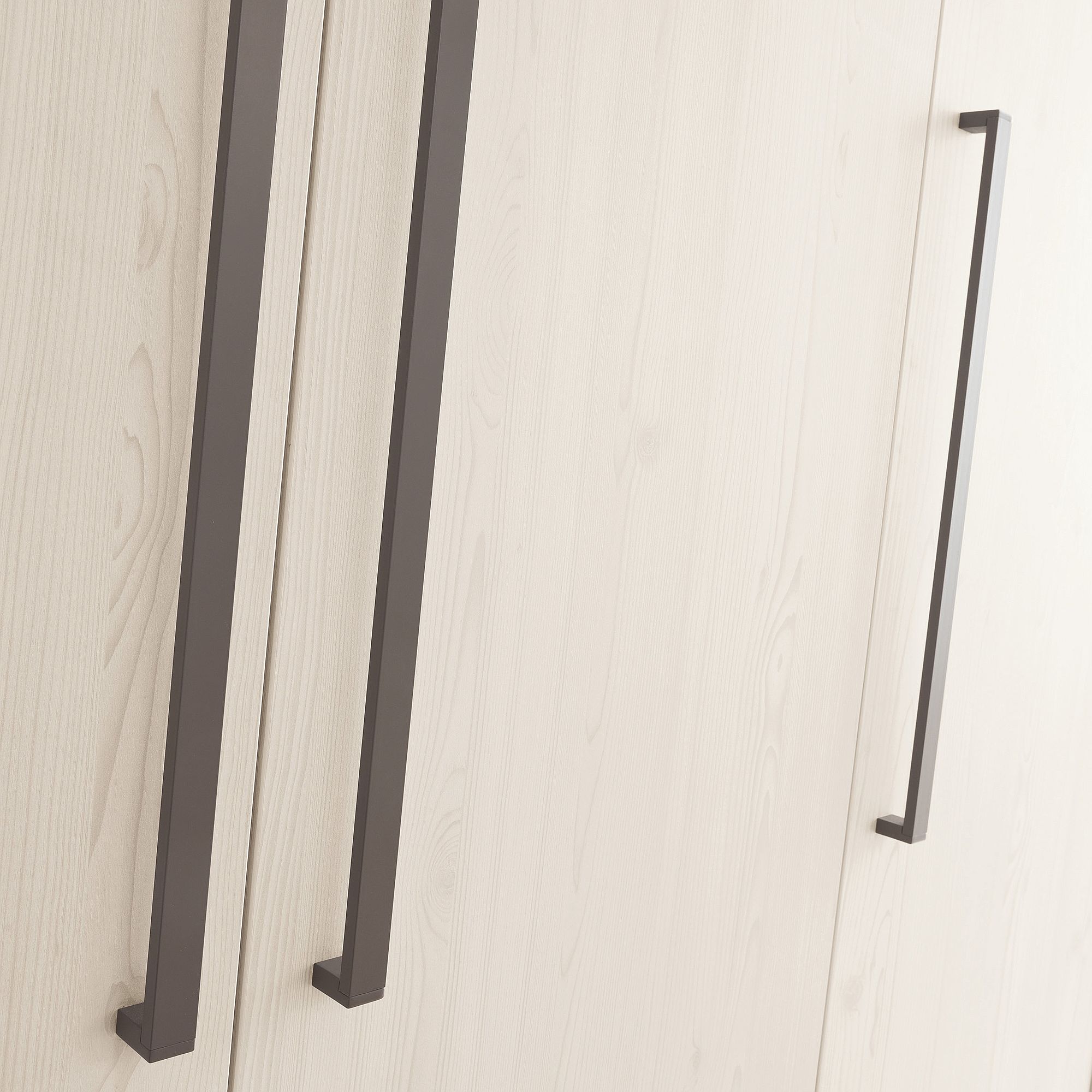 Drehtürenschrank Laslo mit 3 Türen und 1 Schublade Drei lange, schwarze Griffe an Schranktüren aus hellem Holz.