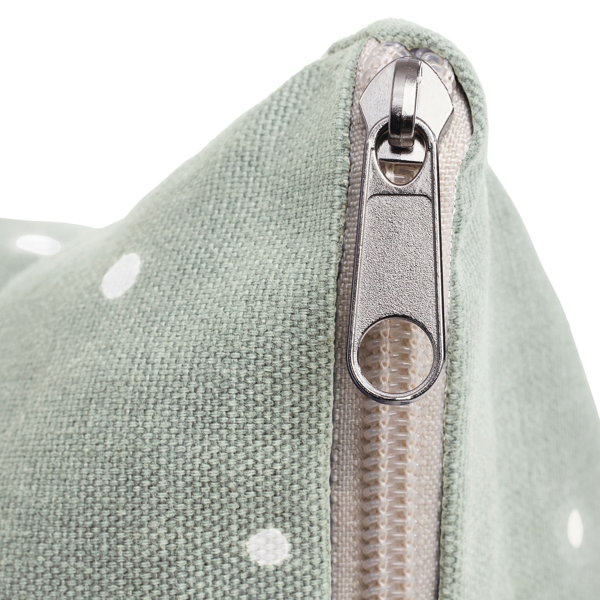 Nahaufnahme eines silbernen Reißverschlusses auf einer hellgrünen Stofftasche mit weißen Punkten.