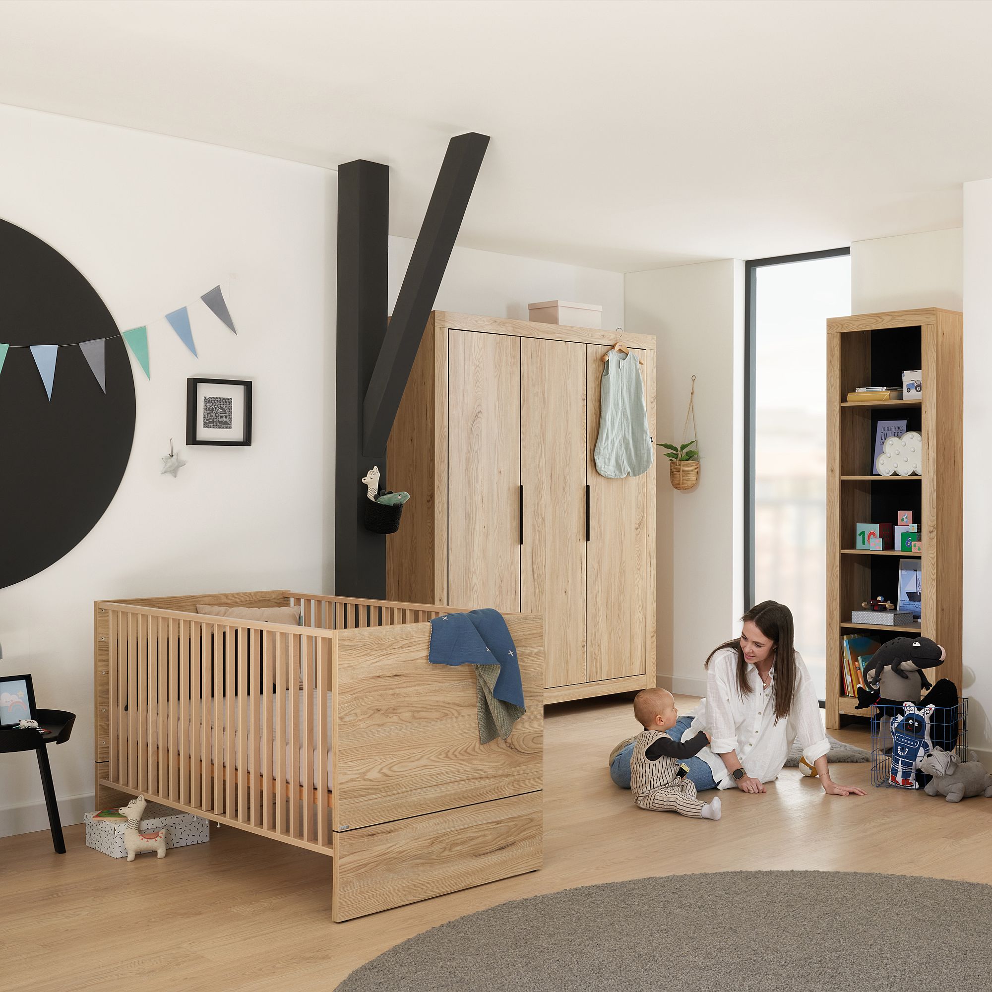 Eine Frau sitzt mit einem Baby in einem modernen, gemütlichen Kinderzimmer auf dem Boden.