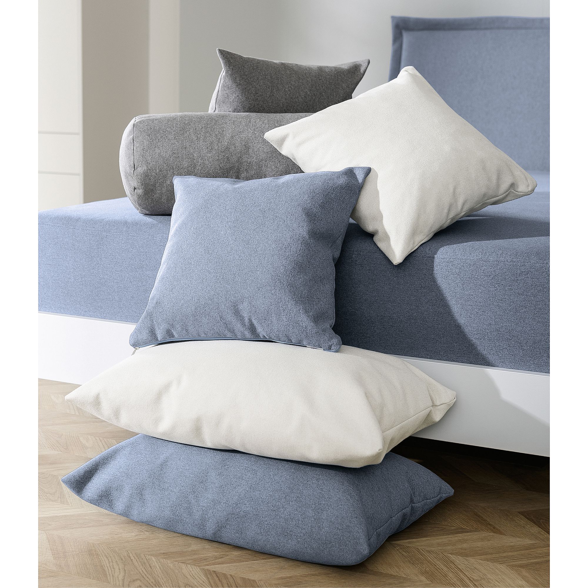 Stacked blue, gray, and white pillows on and beside a bed with blue bedding.