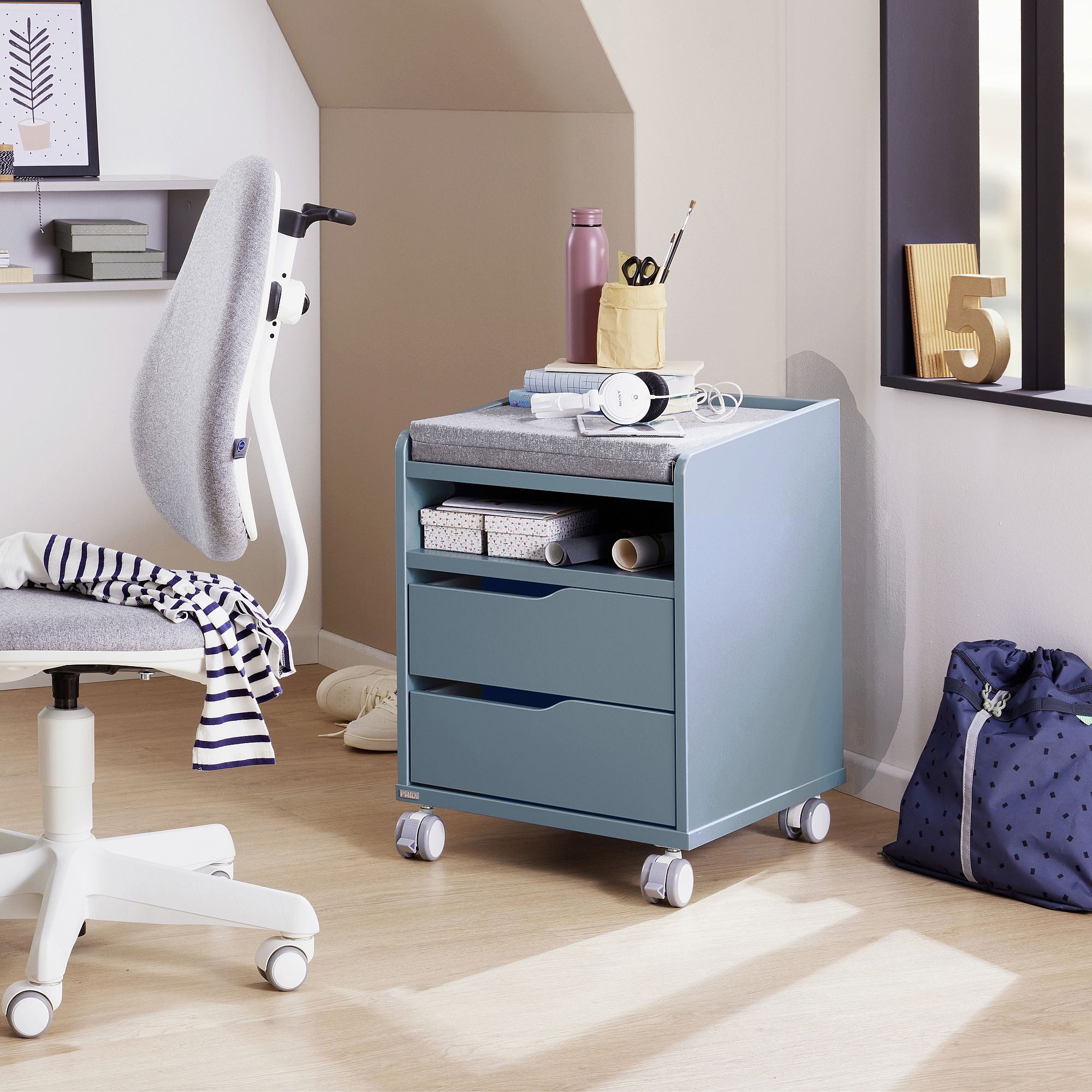 A blue rolling drawer unit beside a chair in a bright, modern study room.